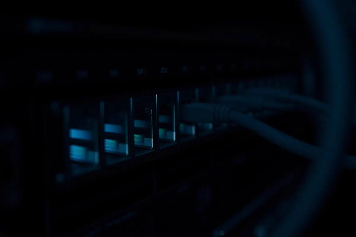 Extreme close-up of network switch faceplate with rows of plugged ethernet cables and glowing cyan and teal port activity indicators